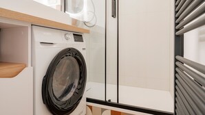 Un'area lavanderia moderna con una lavatrice Valberg, un piano di lavoro in legno e una porta in vetro.