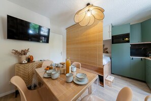 A modern kitchen with a built-in oven, a dining area with a wooden table and chairs, and a TV mounted on the wall. - Les Cimes d'Hestia - Proche station de ski (La Salle-les-Alpes)