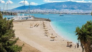 Una playa con sombrillas, una marina con barcos y un paisaje urbano al fondo.