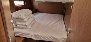 Ein kleines Zimmer mit Holzwänden, einem Fenster und einem kompakten Bett mit weißer Bettwäsche.