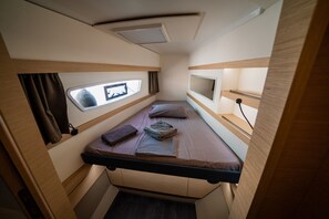 Un intérieur de camping-car compact, avec un seul lit, une fenêtre, un petit téléviseur et une étagère de rangement.