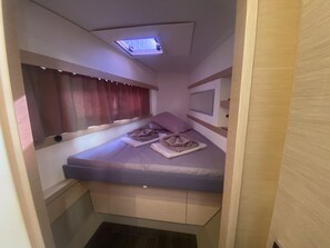 Ein kleiner Raum mit einem Bett, einer Deckenleuchte, einem Fenster mit Vorhängen und einem an der Wand befestigten Fernseher.