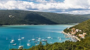 Una cittadina costiera con un porto turistico pieno di vele, circondata da colline e un cielo sereno.