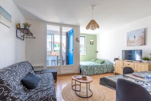 Ein Wohnzimmer mit einer Couch, einem Esstisch, einem Fernseher und einem Bett mit einem grün-floralen Bettüberwurf.