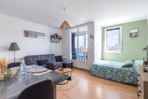 Eine moderne Wohnung mit Sofa, Esstisch, Bett und Blick auf die Stadt.