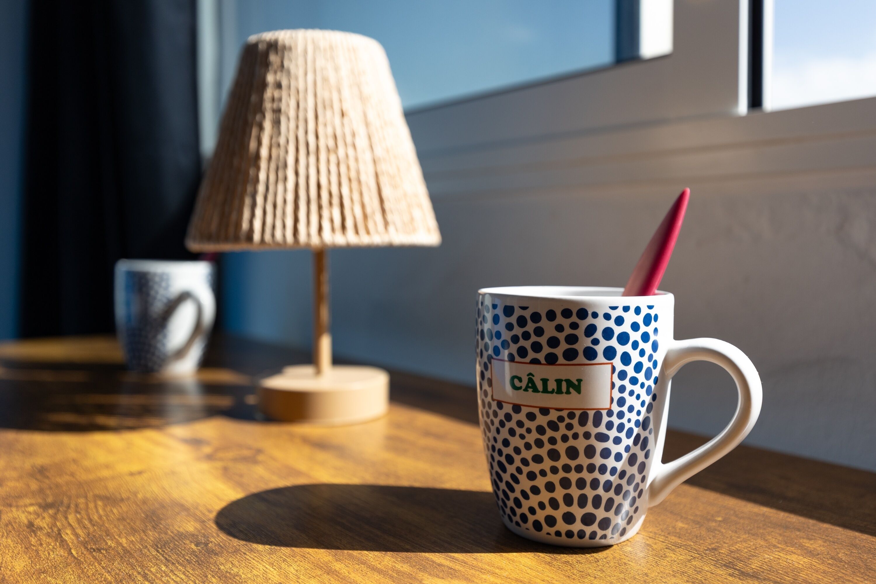 A wooden table with a polka-dotted mug labeled 'CÁLIN' and a lamp.