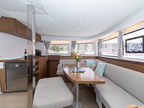 Eine kompakte Küche mit Kühlschrank, eine Essecke mit Tisch und Bank sowie große Fenster mit Blick auf den Hafen.