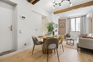 A dining area with a round table, chairs, and a plant. There is a sofa and a TV in the background. - L'Atelier des Remparts - Au cœur du Vieil Antibes (Antibes)