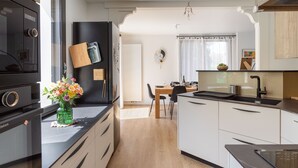 Een moderne keuken met een zwarte koelkast, witte kasten en een houten eettafel.