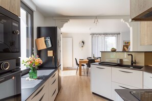 A modern kitchen with a black refrigerator, white cabinets, and a wooden dining table. - Jardin papillons - À moins d'1 km de la plage (Erquy)