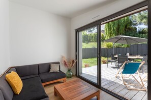 A modern living room with a sofa, coffee table, and sliding glass door leading to an outdoor patio area. - Jardin papillons - À moins d'1 km de la plage (Erquy)