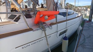 Un yacht blanc, baptisé SUN ODYSSEY 19, était amarré dans une marina, avec des cordes, un gilet de sauvetage et un panneau de commande.