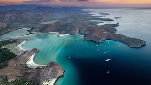 Vue aérienne d’une zone côtière avec des eaux turquoise limpides, un terrain rocheux et plusieurs bateaux.
