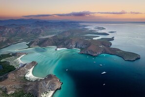 Eine Luftaufnahme einer Küstenregion mit klarem türkisblauem Wasser, felsigem Gelände und mehreren Booten.