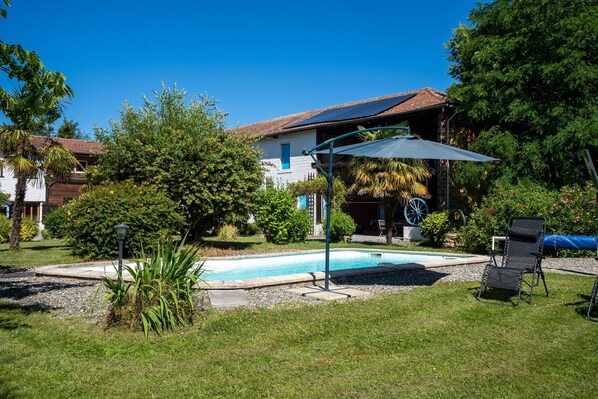 Um quintal com piscina, um espaço de área coberta e uma casa com telhado cerâmico.