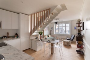 Eine moderne Küche mit Marmorarbeitsplatte, einer Holztreppe und einem Essbereich mit klaren Stühlen.