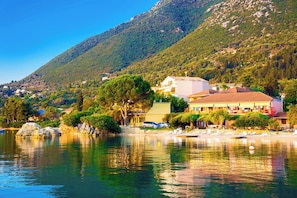 A coastal hotel with a mountain backdrop, a beach, and a calm lake. - Sun-Kissed Sailing Adventure in the Ionian Islands (Nikiana)