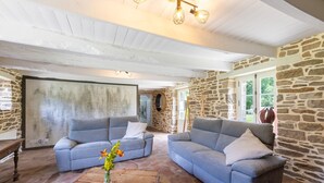 Una habitación con dos sofás grises, una mesa de centro de madera con un jarrón de flores, paredes de piedra y un techo blanco.