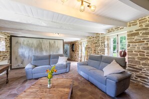 A room with two grey sofas, a wooden coffee table with a vase of flowers, stone walls, and a white ceiling. - La Chaumière BZH - Pour 5 avec grand jardin (Riec-sur-Bélon)