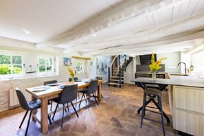 A spacious kitchen with a dining area, stone flooring, and a staircase leading to an upper level. - La Chaumière BZH - Pour 5 avec grand jardin (Riec-sur-Bélon)