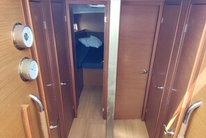 Un couloir étroit avec des portes en bois, un lit avec un oreiller blanc et deux horloges murales.