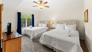 A hotel room with two beds, a ceiling fan, a TV on a wooden desk, and a window with curtains. - 2BR Legends Golf Villa - Ground Floor - Pond View (Myrtle Beach)