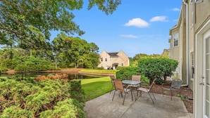 A house with a pond, a patio with chairs, and a well-maintained lawn. - 2BR Legends Golf Villa - Ground Floor - Pond View (Myrtle Beach)