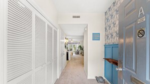 A hallway with white louvered closets, a blue door with a 'NO SPIKES PLEASE' sign, and a carpeted floor. - 2BR Legends Golf Villa - Ground Floor - Pond View (Myrtle Beach)