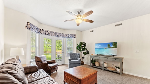 A living room with a ceiling fan, a TV, a sofa, a coffee table, and a plant. - 2BR Legends Golf Villa - Ground Floor - Pond View (Myrtle Beach)