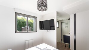 A modern bedroom with a bed, a TV mounted on the wall, a window, and a view of the garden. - La Corniche - Belle maison pour 6 avec vue mer (Cancale)