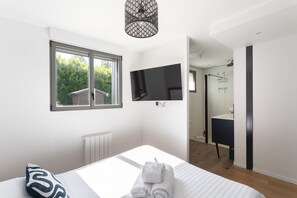 A modern bedroom with a bed, a TV mounted on the wall, a window, and a view of the garden. - La Corniche - Belle maison pour 6 avec vue mer (Cancale)