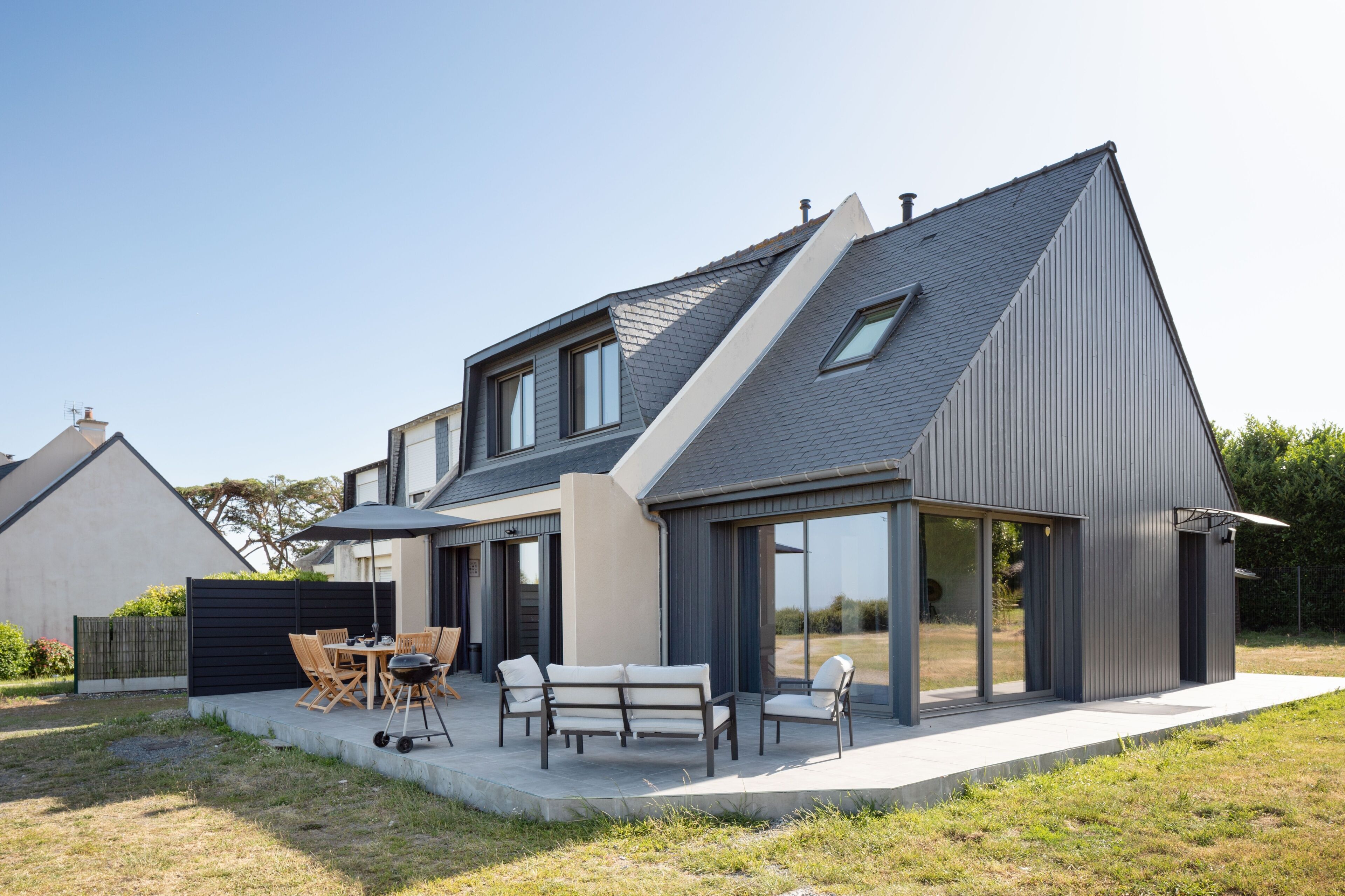 Una casa moderna con un patio, mobiliario exterior y un gran ventanal.