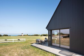 A modern building with a patio area, large windows, and a view of the landscape. - La Corniche - Belle maison pour 6 avec vue mer (Cancale)