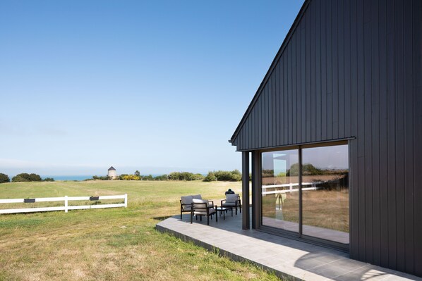 A modern building with a patio area, large windows, and a view of the landscape. - La Corniche - Belle maison pour 6 avec vue mer (Cancale)