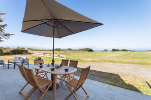 An outdoor patio with a round table, wooden chairs, and a large umbrella. - La Corniche - Belle maison pour 6 avec vue mer (Cancale)