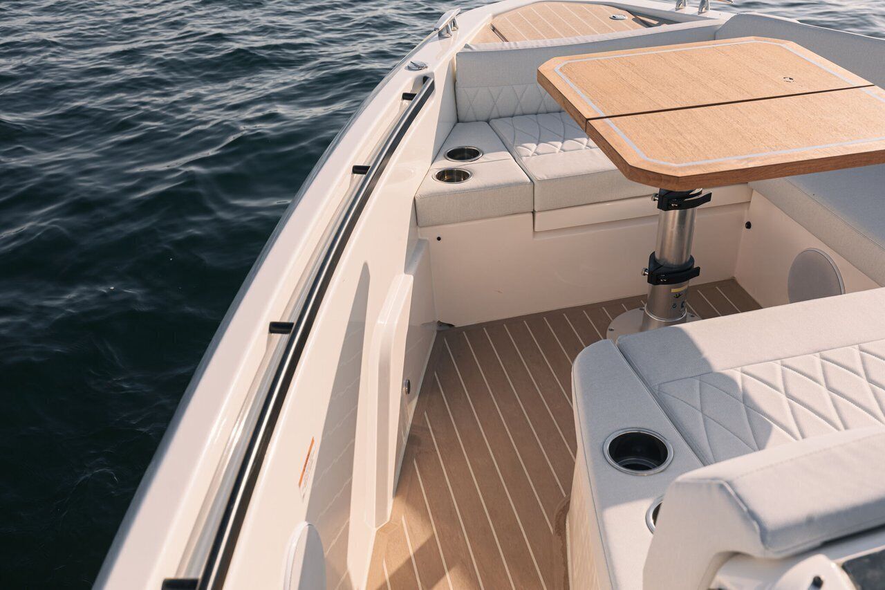 A boat interior with a cushioned seating area, a wooden table, and a metal railing.