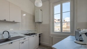 Una cocina moderna con armarios blancos, encimera de mármol, estufa integrada y ventana con vistas a edificios.