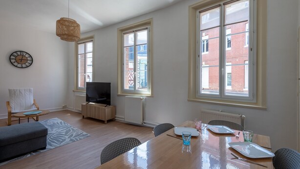 Una sala de estar moderna con una mesa de comedor de madera, un televisor y un ventanal grande.