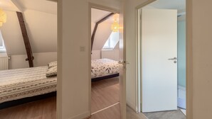 Un dormitorio con una cama, una escalera de madera, una ventana y una puerta que da a otra habitación.