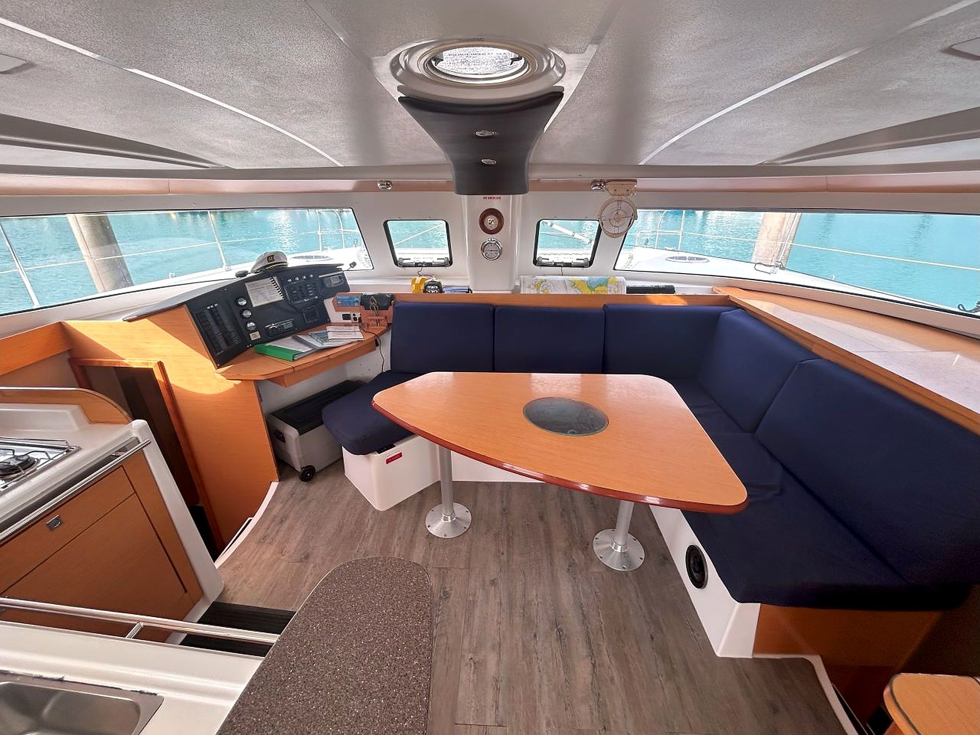 A boat's interior with a control station, seating area, and windows offering a view of the water.