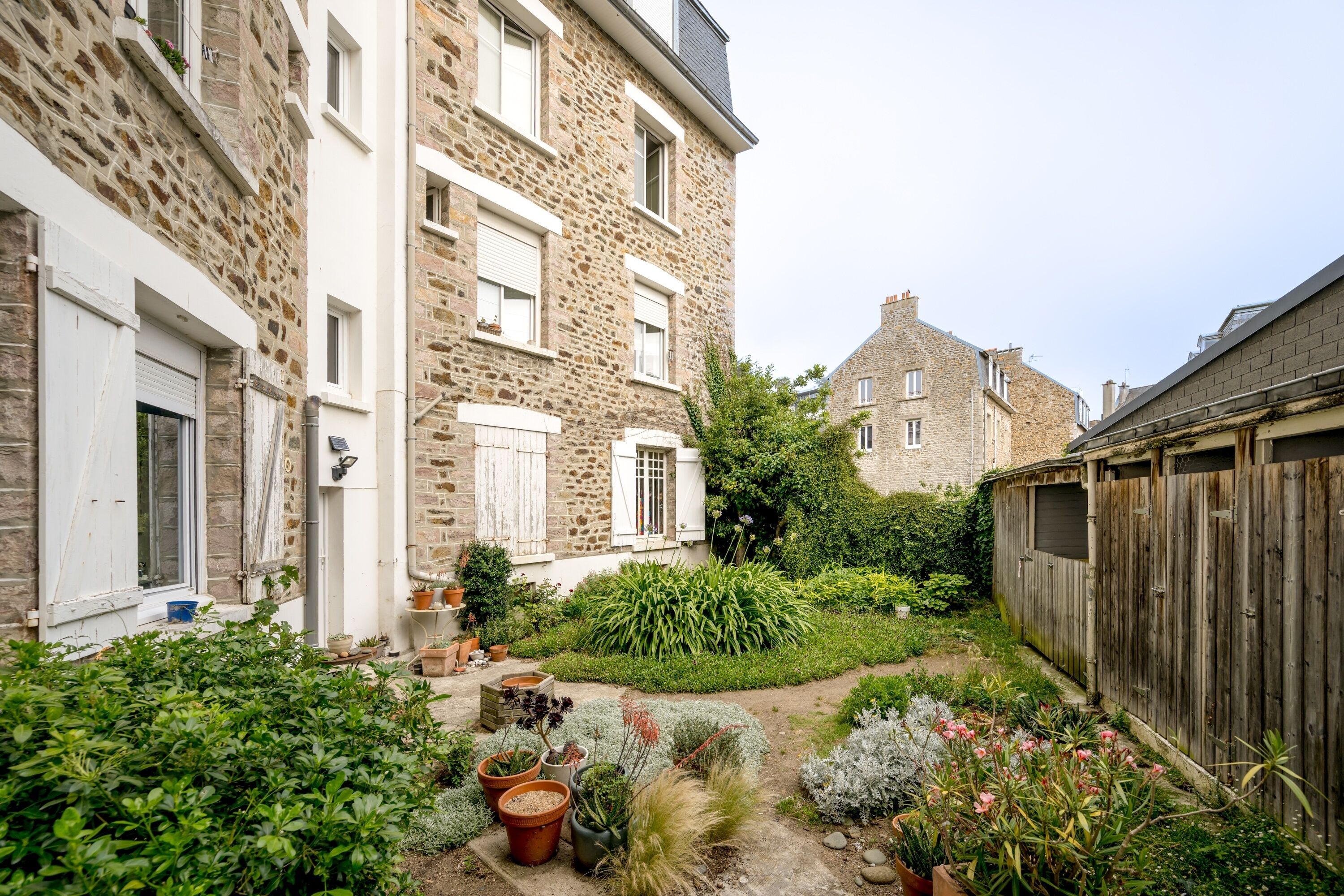 A courtyard with stone buildings, potted plants, and a wooden fence.