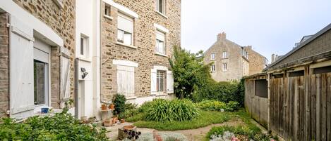 A courtyard with stone buildings, potted plants, and a wooden fence.