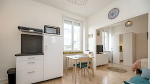 Ein kompakter Wohnraum mit Küchenzeile, Essbereich, einem Bett und Blick durch ein großes Fenster.