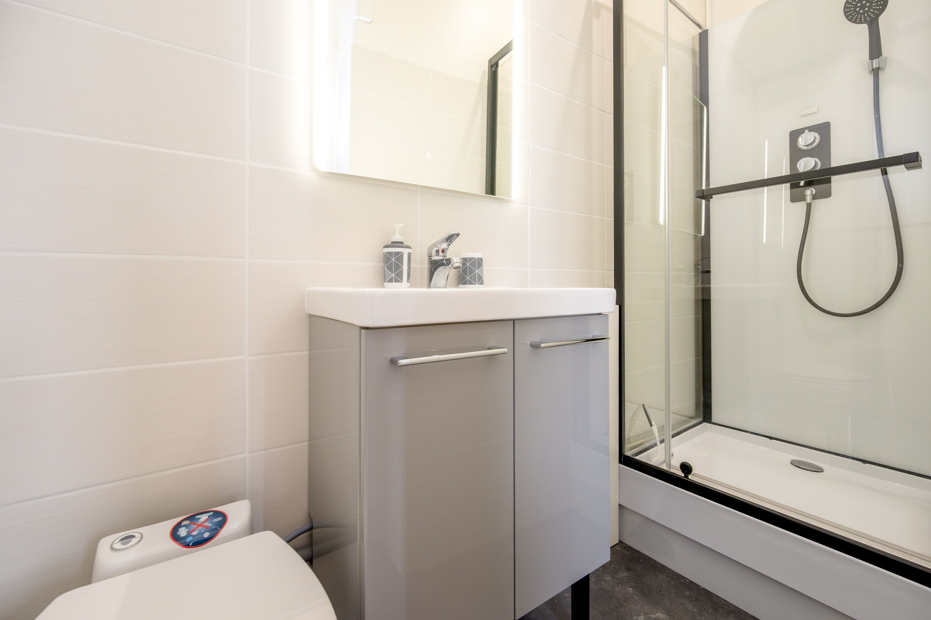 A modern bathroom with a glass shower enclosure, a white sink with a mirror, and a toilet with a safety lock.