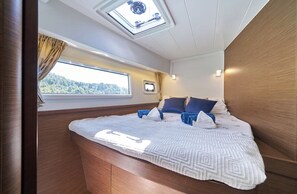 Ein kleines Schlafzimmer mit Bett, Oberlicht, Fenster und einem kleinen Nachttisch.