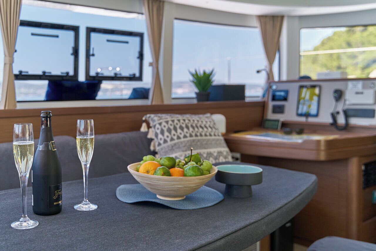 A dining area with a table, two wine glasses, a bottle, and a bowl of fruit.
