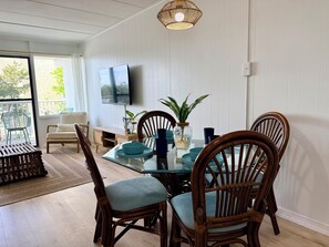 A dining area with a glass table, wicker chairs, and a TV mounted on the wall. - Oceanside Condo - Sleeps 6 - Beach Gear - Parking (Ocean City)