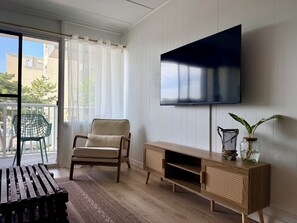 A living room with a TV, a chair, a wooden cabinet, and a balcony with a chair. - Oceanside Condo - Sleeps 6 - Beach Gear - Parking (Ocean City)