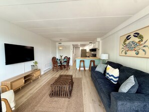 Ein Wohnzimmer mit Fernseher, Holzmöbeln, einer Couch und einer Küche im Hintergrund.