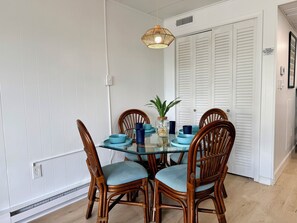 Een eetgedeelte met een glazen tafel, rieten stoelen en een hanglamp.